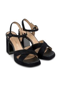 Czarne zamszowe sandały na wysokim obcasie z odkrytym palcem, przeplatane paski i kwadratowy blokowy obcas. Wkładka jest beżowa z subtelnym brandingiem.