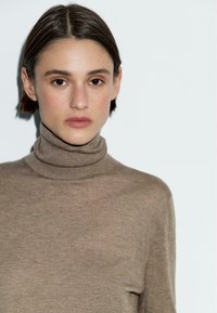 Beżowy sweter z golfem wykonany z miękkiego, teksturowanego materiału. Dopasowany fason z wysokim kołnierzem i długimi rękawami. Prosty, minimalistyczny styl.