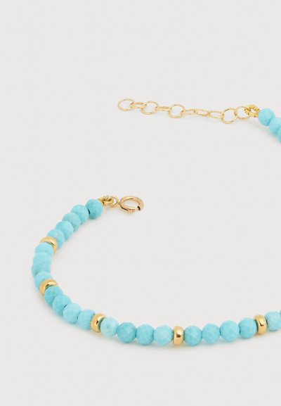 Βραχιόλι με τυρκουάζ χάντρες, μικρές χρυσές αποστάτες και χρυσή ρυθμιζόμενη αλυσίδα με κούμπωμα σε λευκό φόντο.