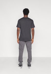 Camiseta gris de manga corta, combinada con pantalones cargo grises con bolsillos laterales, llevada con zapatillas deportivas negras.