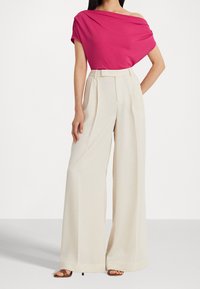 Fuchsia av-axeln topp i kombination med krämfärgade vida byxor med en skräddarsydd midja och en mjuk tygtextur.
