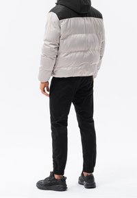 Puffer jacket in light gray with a black hood, paired with black jogger pants, and black sneakers. Smooth texture, athletic fit.