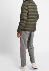 Puffjacka i olivgrön färg, med horisontell quiltad design, hög krage och logotypdetalj på ärmen. Kombinerad med gråa joggers.