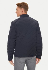 Giacca a vento blu navy con cuciture a zig-zag, colletto alto e texture liscia. Presenta un design aderente e maniche leggermente imbottite.
