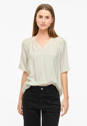 Haut crème à manches courtes avec un col en V et des détails en dentelle sur les épaules, associé à un jean noir taille haute. Tissu doux et léger.