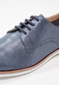 Scarpa da uomo in pelle blu perforata con una superficie liscia, punta rotonda, chiusura con lacci e suola in gomma bianca.