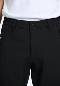 Czarne spodnie z gładkiego, elastycznego materiału. Posiadają kieszeń na zamek, zapięcie na guzik i paski na pasek. Minimalistyczny design, dopasowany krój.