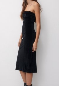 Vestido midi negro sin tirantes, hecho de suave tela de terciopelo, que presenta un corsé ajustado y una falda acampanada y lisa con un dobladillo justo debajo de la rodilla.