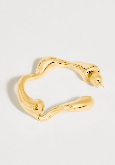 Gold-tone metal hoop earring with an irregular, wavy shape and a post back fastening on a white background.