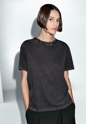 T-shirt nera oversize realizzata in tessuto morbido con una texture leggermente sbiadita. Presenta un colletto rotondo e maniche corte con bordi grezzi.