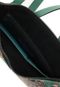 Interno di una borsa a tracolla in pelle verde con fodera in tessuto nero, dotato di una tasca con zip e uno scomparto per carte color turchese. Chiusura con zip visibile.