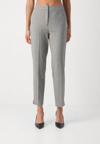 Pantalon à carreaux gris avec une coupe ajustée, présentant une taille haute, une texture subtile et des détails de coutures latérales, associé à des talons noirs pointus.