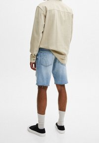 Vaaleanbeige pitkähihaisten paita, rento malli, jossa napitettava hihansuu. Yhdistetty vaalensinisiin kulutettuihin farkkushortseihin, joissa on revitty helma, ja mustiin lenkkareihin.