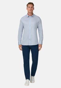 Himmelblaues Langarmhemd mit Knopfleiste und Kragen, kombiniert mit dunklen Jeans und weißen Sneakers. Glatte Stofftextur.