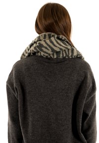 Gebreide infinity sjaal met een gestructureerd lichtgrijs en donkergroen zebrapatroon, om de hals gewikkeld, gecombineerd met een donkere trui.