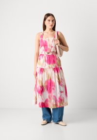 Robe avec un décolleté carré, motif floral rose et beige, jupe à volants et taille ceinturée. Associée à un jean ample et des chaussures neutres.