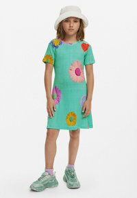 Turkos klänning med korta ärmar pryds av färgglada blomapplikationer, inklusive masker och accenter i lila, gult och rött. Tyget är en blandning av bomull.