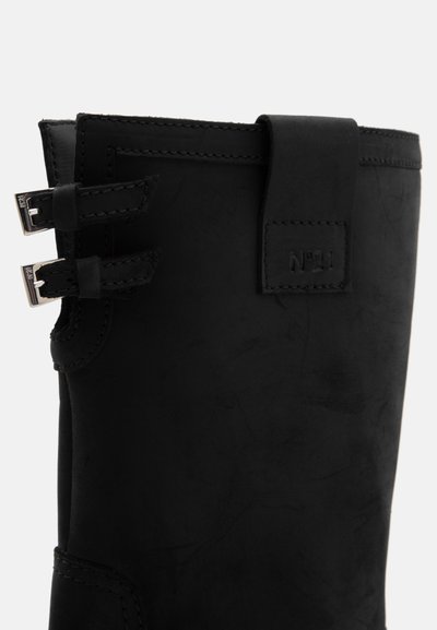 Botas de cuero negro con una textura suave, forma redondeada y dos correas ajustables con hebillas metálicas a los lados.