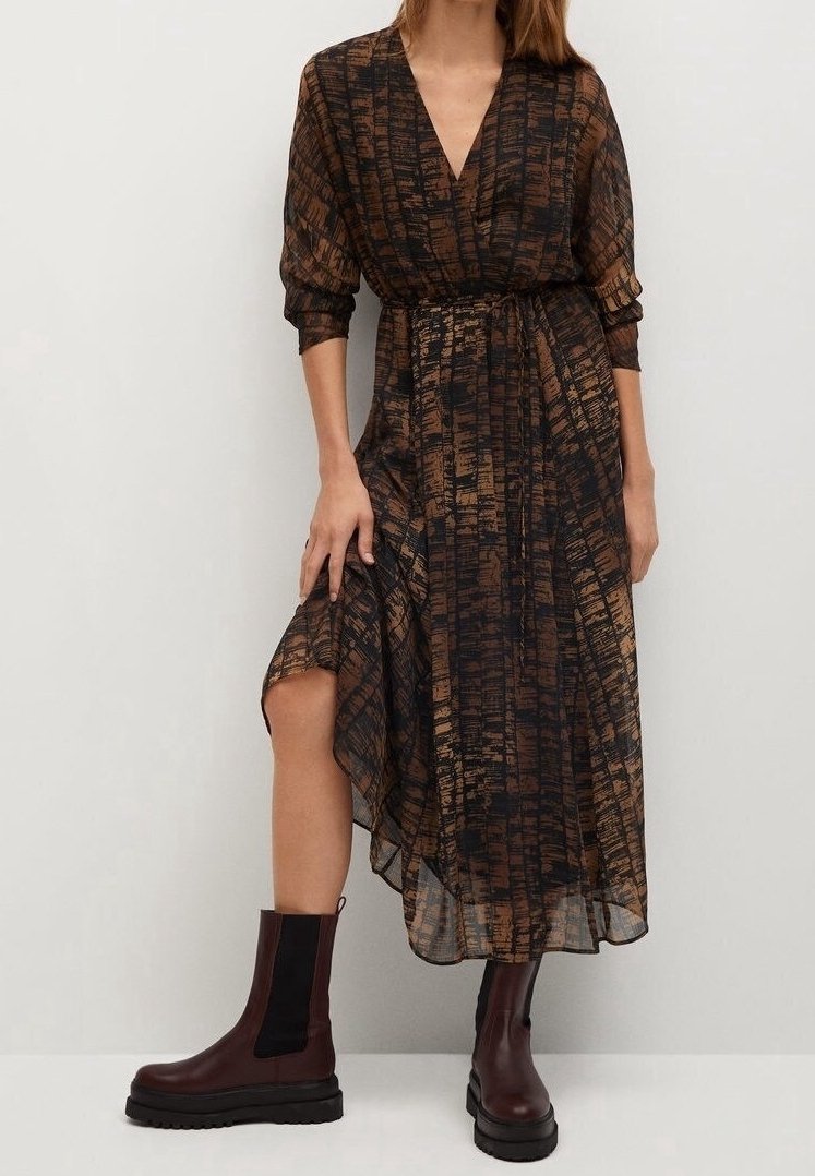 Braun gemustertes Wickelkleid mit langen Ärmeln, asymmetrischem Saum und einem Gürtel in der Taille, kombiniert mit dunkelbraunen Stiefeletten.
