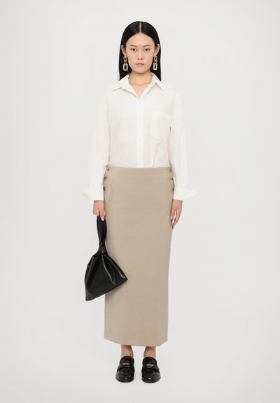 Hvid skjorte med krave, beige nederdel med sidelukninger, sort lædertaske. Modellen bærer sorte loafers med guldkante.