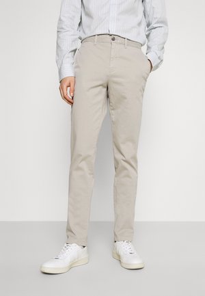 Beige bomullschinos med slim fit, med knäppning och framfickor, i kombination med vita sneakers. En vertikalt randig skjorta syns.