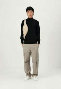 Cămașă neagră cu mânecă lungă, geantă bej tip crossbody, pantaloni cargo gri și adidași albi. Design simplu, texturi din bumbac și detalii funcționale.