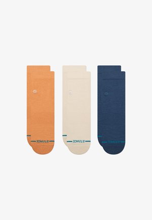 Tres pares de calcetines en naranja, crema y azul marino, con una textura suave, diseño acanalado y una marca de contraste en turquesa en los puños.