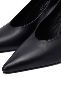 Zapatos negros de piel con punta afilada y textura suave. Cuentan con un diseño de corte bajo y un acabado brillante. Sin herrajes ni patrones visibles.