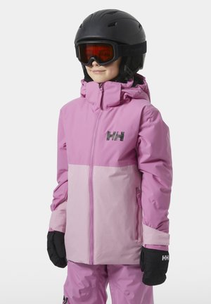 Bambino che indossa una giacca da sci bicolore rosa, pantaloni abbinati, guanti neri, casco nero e occhiali da sci arancioni, in piedi su sfondo bianco.