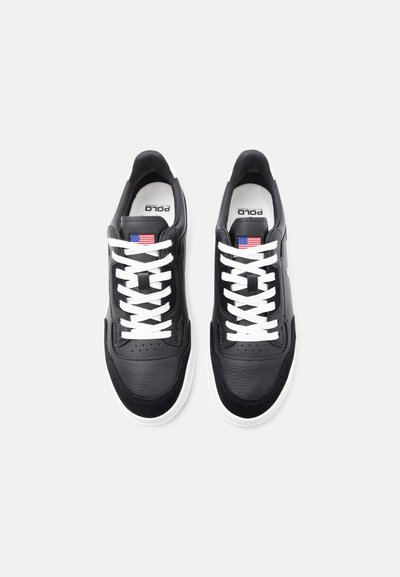 Ζευγάρι μαύρα δερμάτινα αθλητικά παπούτσια με λευκά κορδόνια, λευκές σόλες και ταμπελάκια με τη σημαία των Ηνωμένων Πολιτειών στα γλωσσίδια, φαίνονται από πάνω σε λευκό φόντο.