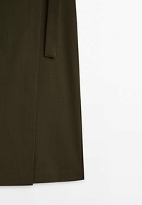 Jupe vert olive foncé avec une fente avant et une ceinture en tissu suspendue sur un fond blanc.