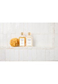 Éponge de mer naturelle avec bouteilles de shampooing et après-shampooing classique Rahua sur une étagère de douche carrelée blanche.