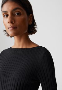 Schwarzes geripptes Langarmoberteil mit Rundhalsausschnitt und strukturiertem Stoff, das ein figurbetontes Design präsentiert.