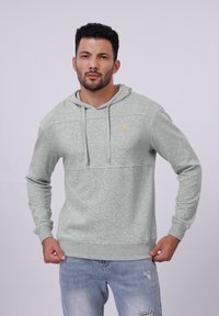 Sudadera con capucha gris de acabado texturizado, con bolsillo tipo canguro y detalle de logo amarillo. Diseñada con capucha ajustable y puños de canalé.