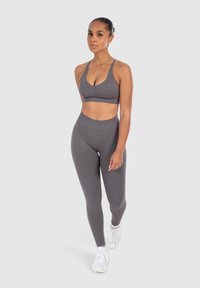 Grau Sport-BH und Leggings-Set aus strukturiertem Stoff. Der BH hat einen runden Ausschnitt und dünne Träger, während die Leggings hochgeschnitten sind.