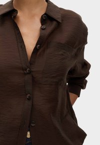 Bruine button-up shirt met een gestructureerde stof, een borstzak en opgerolde mouwen. Heeft donkere knopen en een kraag.