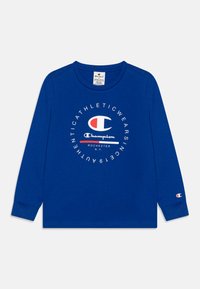 Camiseta de manga larga en algodón azul con un logo circular de Champion en blanco y rojo. Presenta un cuello redondo y puños acanalados.