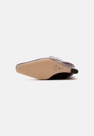 Une chaussure à talon en cuir marron unique couchée sur le côté montrant une semelle beige lisse de taille 38 avec des marquages de la marque.