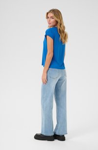 Blue short-sleeve top, relaxed fit, paired with light-wash wide-leg jeans and black flat shoes. Smooth fabric texture, no notable patterns.