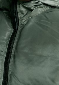 Primo piano di una giacca imbottita verde con zip in plastica nera e cuciture dettagliate lungo le giunture.