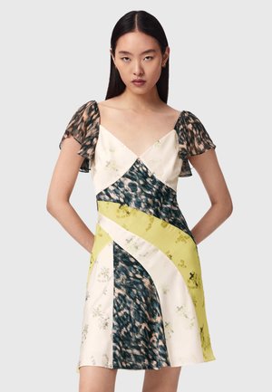 Frau mit glattem schwarzen Haar, die ein kurzärmeliges, V-förmiges Kleid mit gemischten Tier- und Blumenmustern in Creme-, Schwarz- und Gelbtönen trägt.