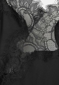 Tela negra con intrincados detalles de encaje, que presenta patrones florales, bordes en forma de ondas y una textura suave, combinando elegancia y suavidad.