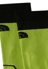 Gröna strumpor med ribbad textur, svarta detaljer upptill och ett enkelt svart grafiskt mönster med ett abstrakt design.