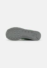 Baskets vertes avec une semelle en caoutchouc gris texturé présentant des crampons profonds pour une meilleure adhérence. Dessus lisse avec des accents subtils, coutures visibles.