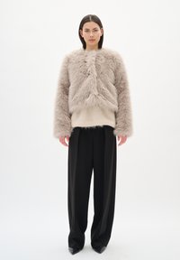 Chaqueta corta de pelaje sintético beige claro con un acabado texturizado y dobladillo acanalado, combinada con pantalones de pierna ancha negros y zapatos de punta negros.