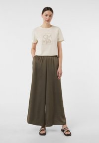 Cream cotton t-shirt featuring a graphic design, paired with lightweight olive wide-leg pants, and black strappy sandals.