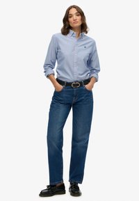 Blauwe en roze gestreepte knoopshirt met een kraag, gecombineerd met donkerblauwe straight-leg jeans en een zwarte riem met een gouden gesp.