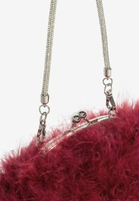 Apsiūtas dirbtinio kailio rankinukas giliomis raudonomis spalvomis, su tekstūruotu, pūkuotu paviršiumi. Sidabrinis metalinis užsegimas ir grandinėlė su dekoratyvinėmis nuorodomis.