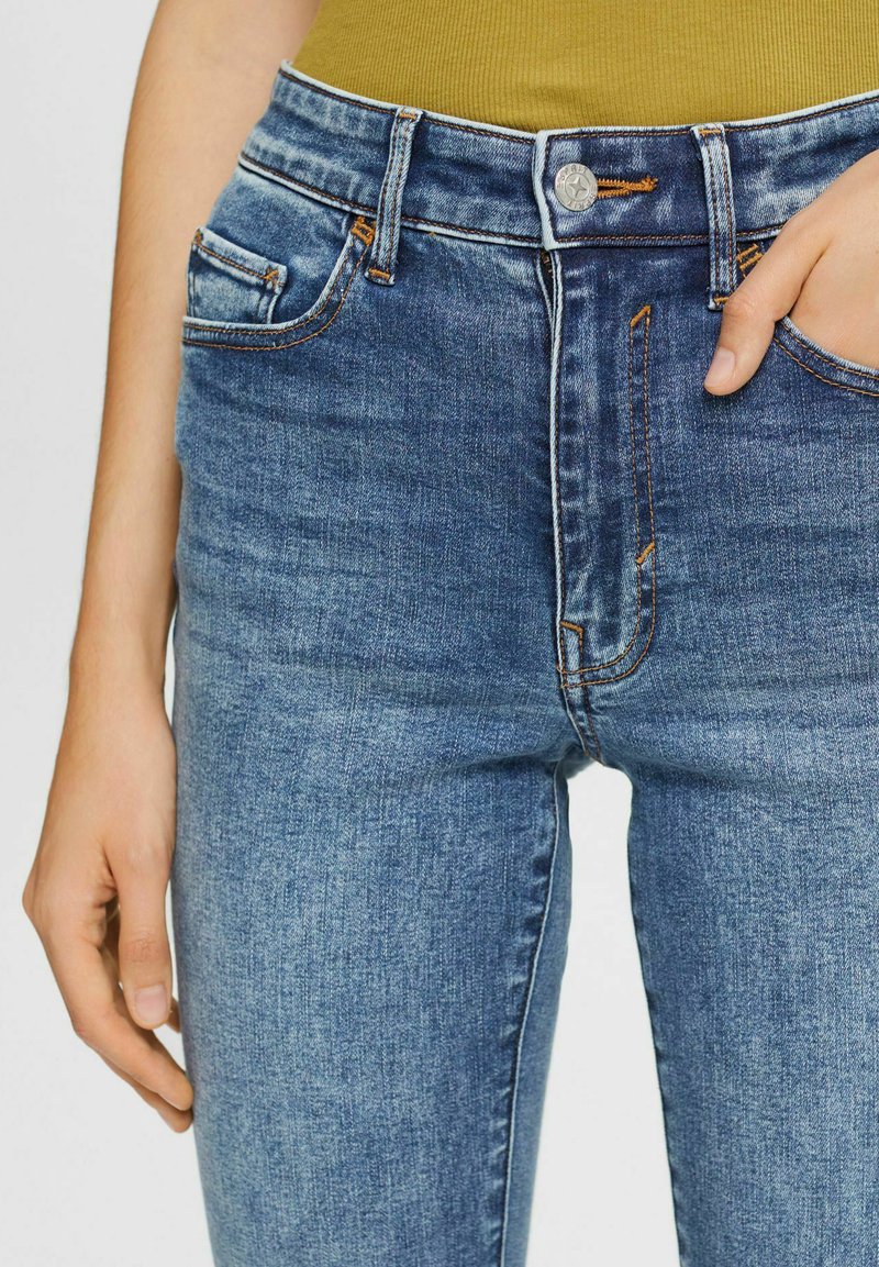 Hoch taillierte blaue Jeans aus Denim mit glatter Textur, kontrastierendem orangefarbenen Nähten und Fronttaschen. Mit einem silbernen Knopfverschluss.