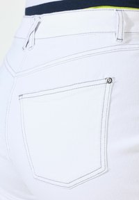Shorts de mezclilla blancos con costuras oscuras en contraste, un bolsillo trasero y un pequeño acento metálico junto al bolsillo. Textura suave.